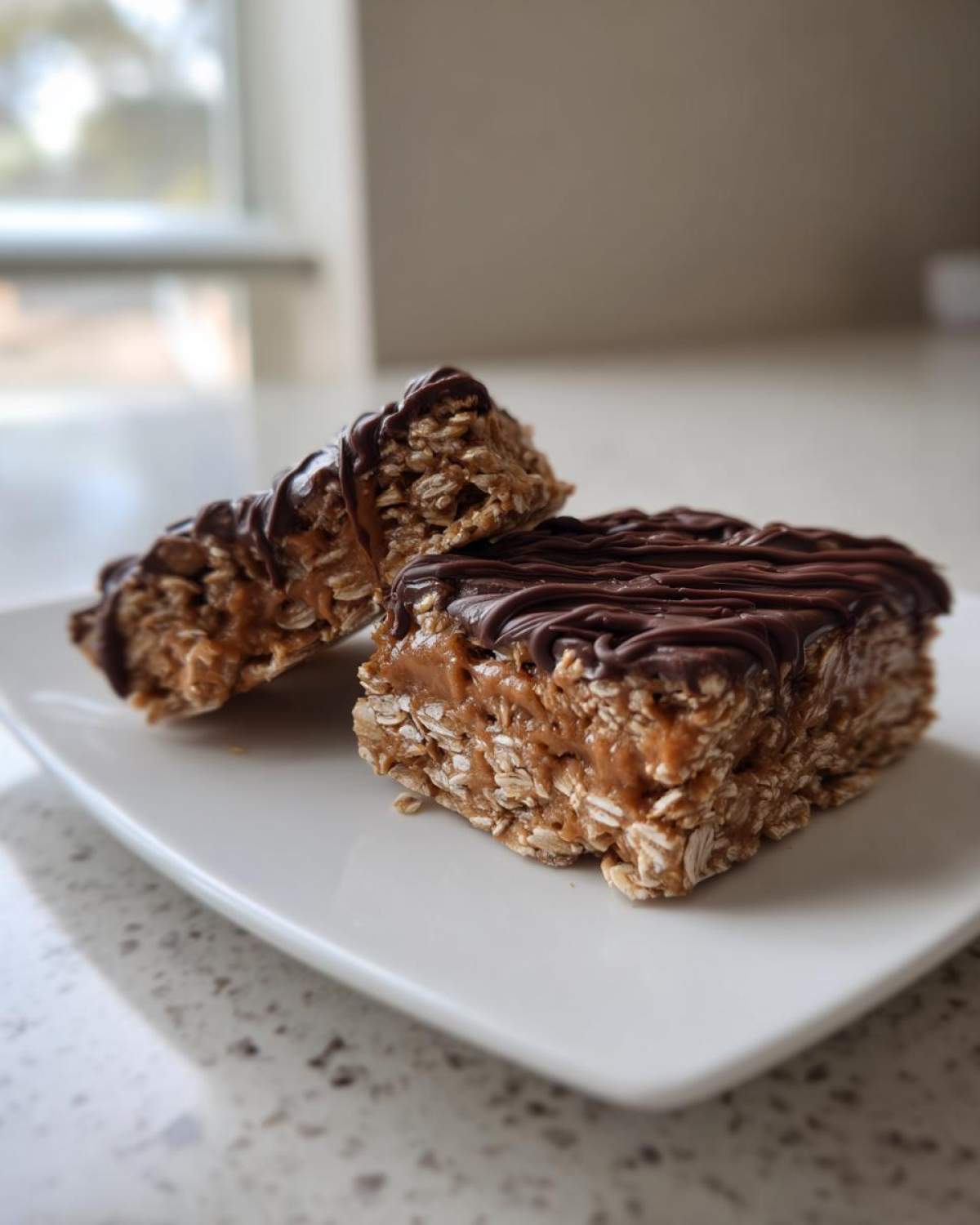 Two pieces of homemade protein bars made with oats and topped with a rich chocolate drizzle, sitting on a white plate.