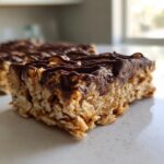 Close-up of a thick, chewy homemade protein bars slice topped with melted dark chocolate and nuts.