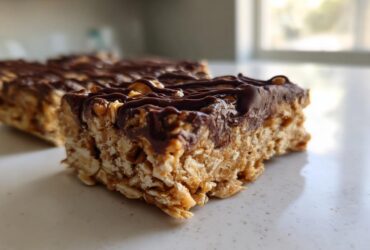 Close-up of a thick, chewy homemade protein bars slice topped with melted dark chocolate and nuts.