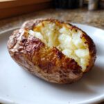 A close-up of a perfectly cooked air fryer baked potato with crispy skin and fluffy interior.