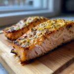 Close-up of a juicy, seasoned air fryer salmon fillet resting on a wooden cutting board.