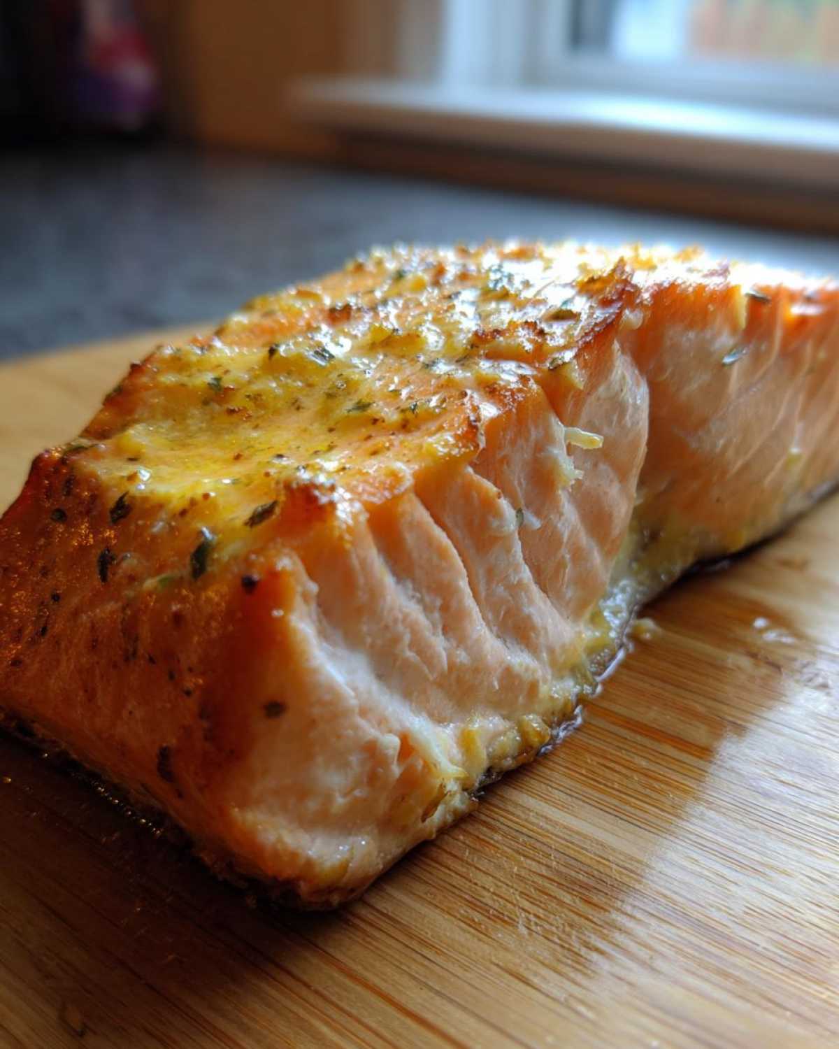 Close-up of a moist, flaky air fryer salmon fillet with a golden-herbed glaze resting on a wooden cutting board.