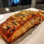 Close-up of a beautifully cooked piece of air fryer salmon with a crispy, golden-brown garlic and herb topping.