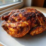 A whole roasted chicken with crispy, seasoned skin resting on a white plate, cooked using an air fryer whole chicken recipe.