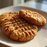 Close-up of three golden brown peanut butter cookies with classic crisscross fork marks resting on a white plate.