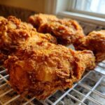 Close-up of several pieces of golden brown, crispy fried chicken resting on a white wire cooling rack.