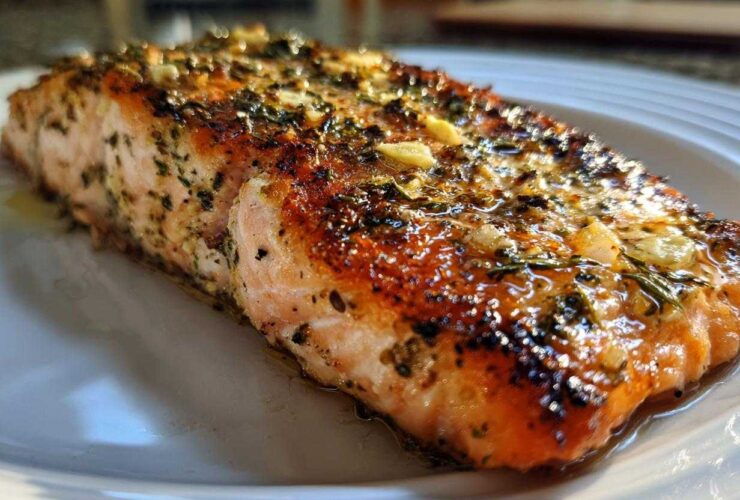 Close-up of a juicy, glazed air fryer salmon fillet topped with garlic and herbs on a white plate.