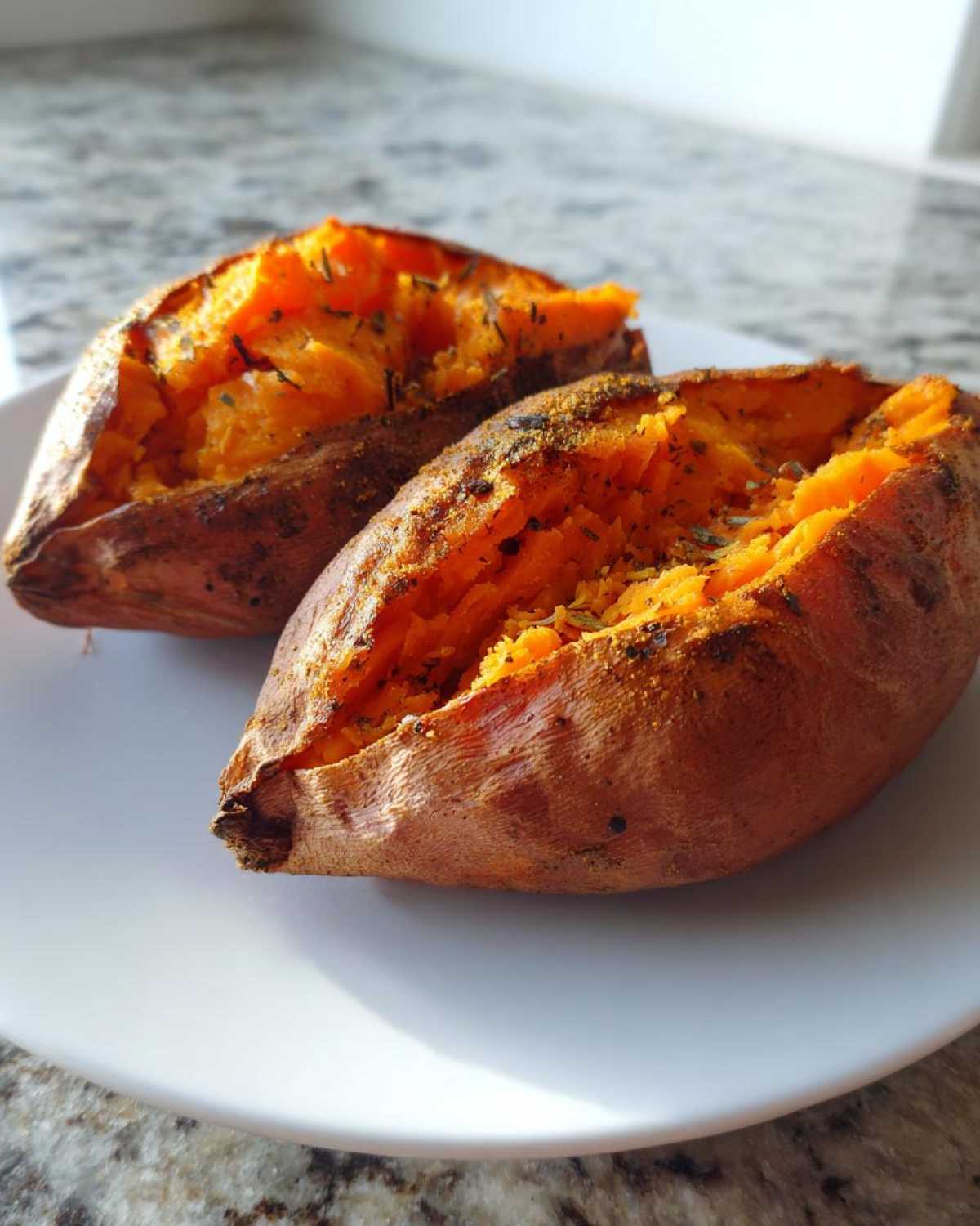 Two halves of a perfectly baked sweet potato, split open and seasoned, resting on a white plate.