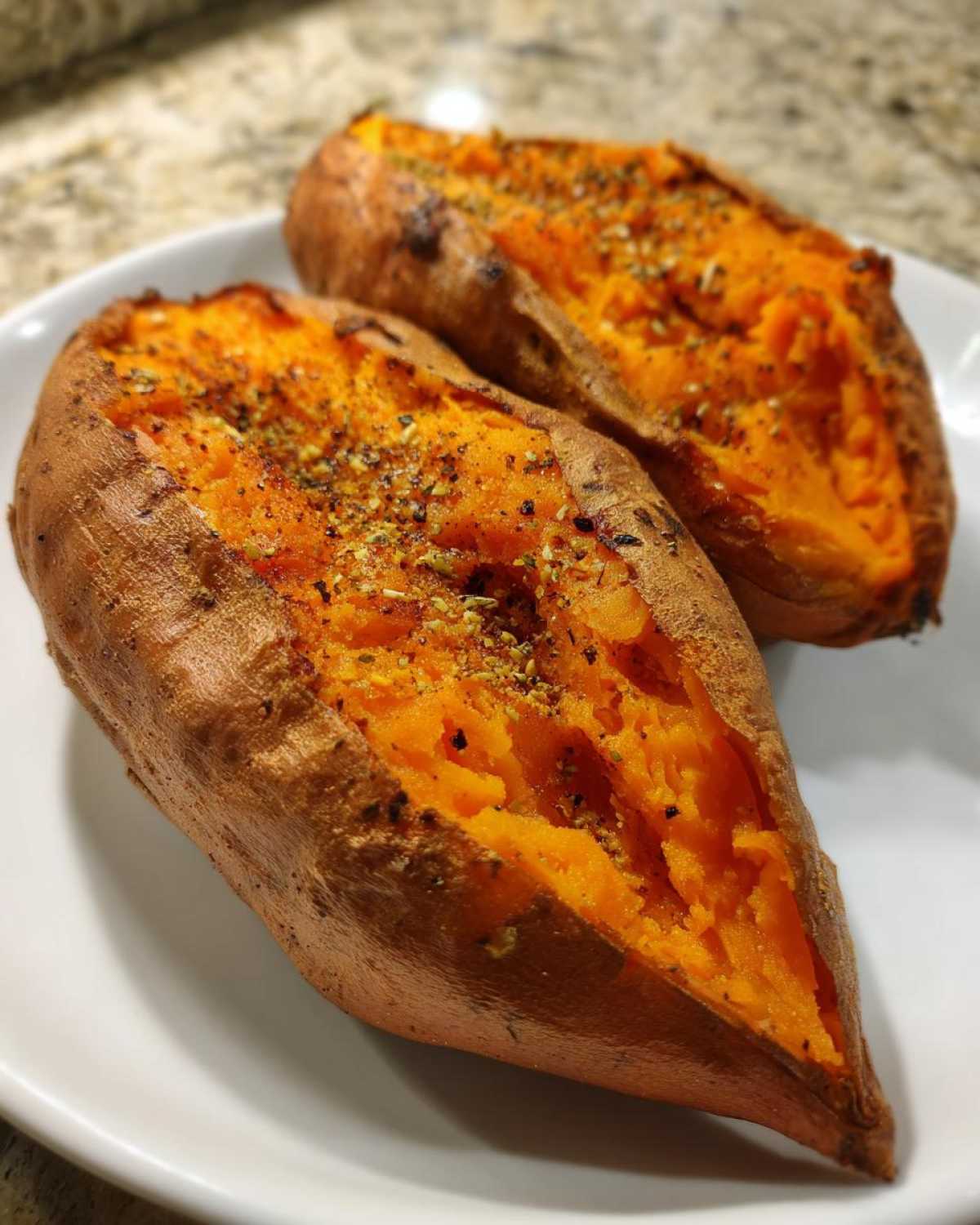 Two halves of a perfectly baked sweet potato, split open and sprinkled with herbs and spices.