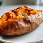 Close-up of a fluffy baked sweet potato, split open and seasoned with pepper and herbs.