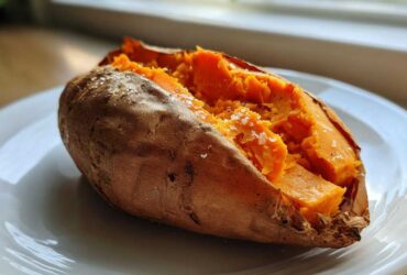 A close-up of a fluffy baked sweet potatoes, split open and sprinkled with coarse sea salt, resting on a white plate.