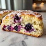 A cross-section of a moist blueberry scones slice, topped with white lemon glaze and coarse sugar.