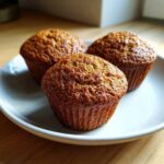 Close-up of three golden brown bran muffins resting on a light blue plate on a wooden surface.