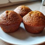 Three golden-brown, freshly baked bran muffins sitting closely together on a white plate.