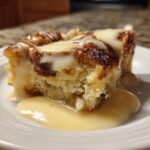 A close-up of a moist slice of bread pudding topped with thick vanilla sauce.