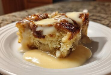 A close-up of a moist slice of bread pudding topped with thick vanilla sauce.