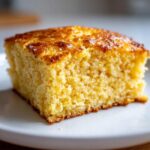 A close-up, appetizing shot of a square slice of moist buttermilk cornbread on a white plate.
