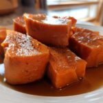 Close-up of thick-cut, glazed candied yams sitting in rich brown syrup on a white plate.