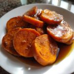 A close-up of thick, glazed slices of amazing candied yams served on a white plate with rich brown syrup.
