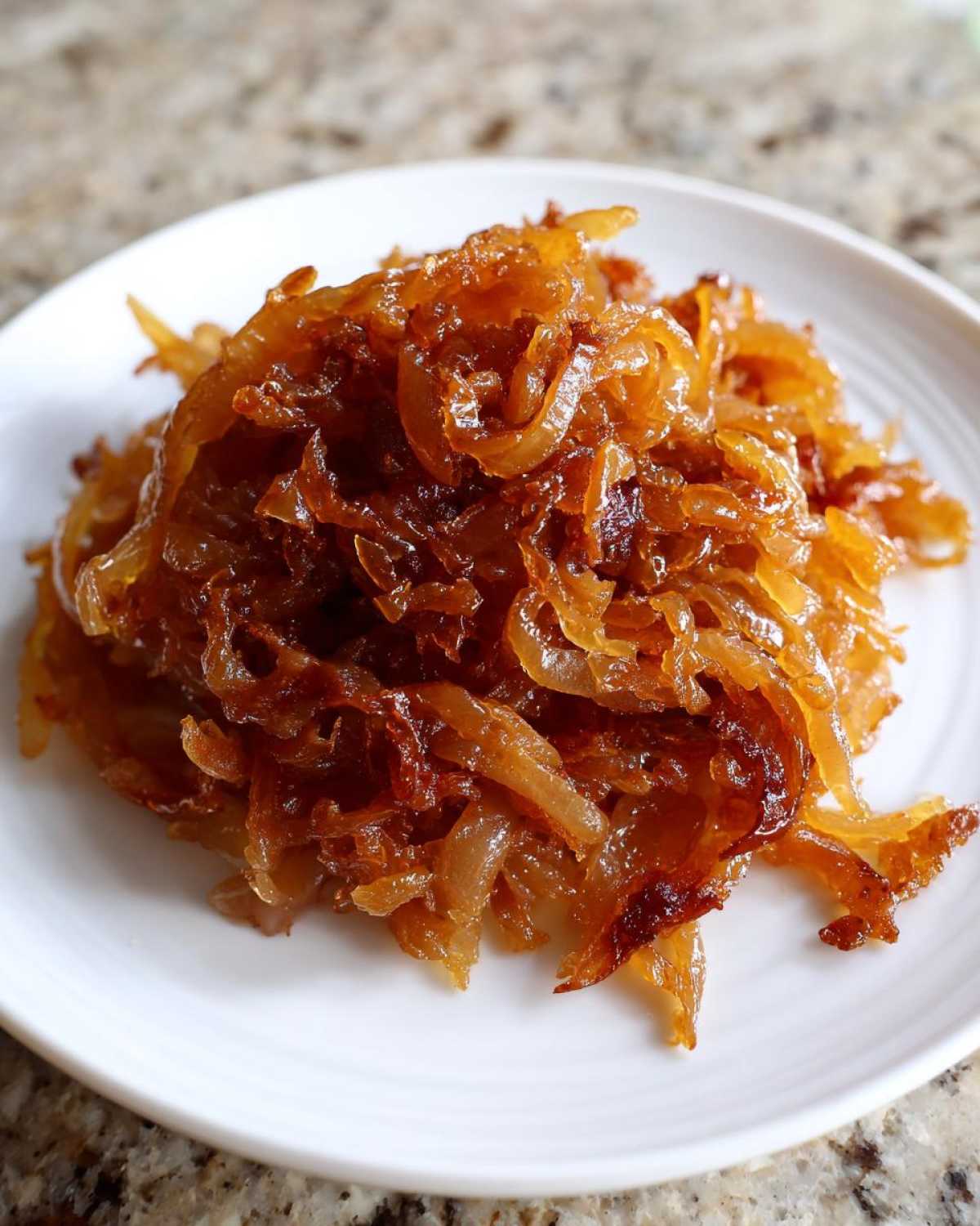 A close-up of rich, deeply browned caramelized onions piled high on a small white plate.