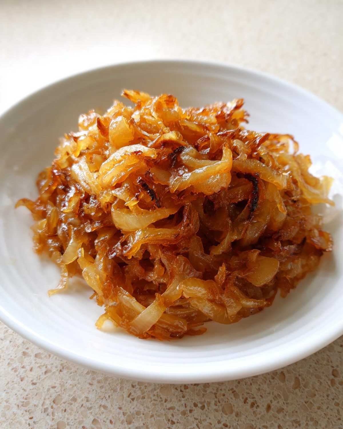 A close-up of deeply golden brown caramelized onions piled high in a small white bowl.