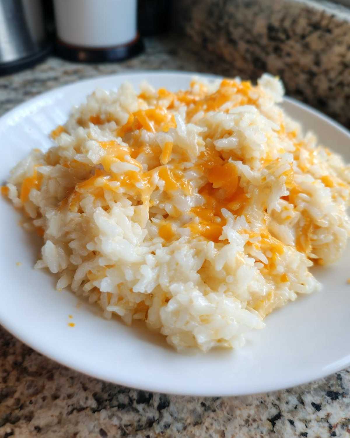 A close-up of creamy white rice mixed with melted orange cheddar cheese, served on a white plate, showcasing the amazing cheesy rice.