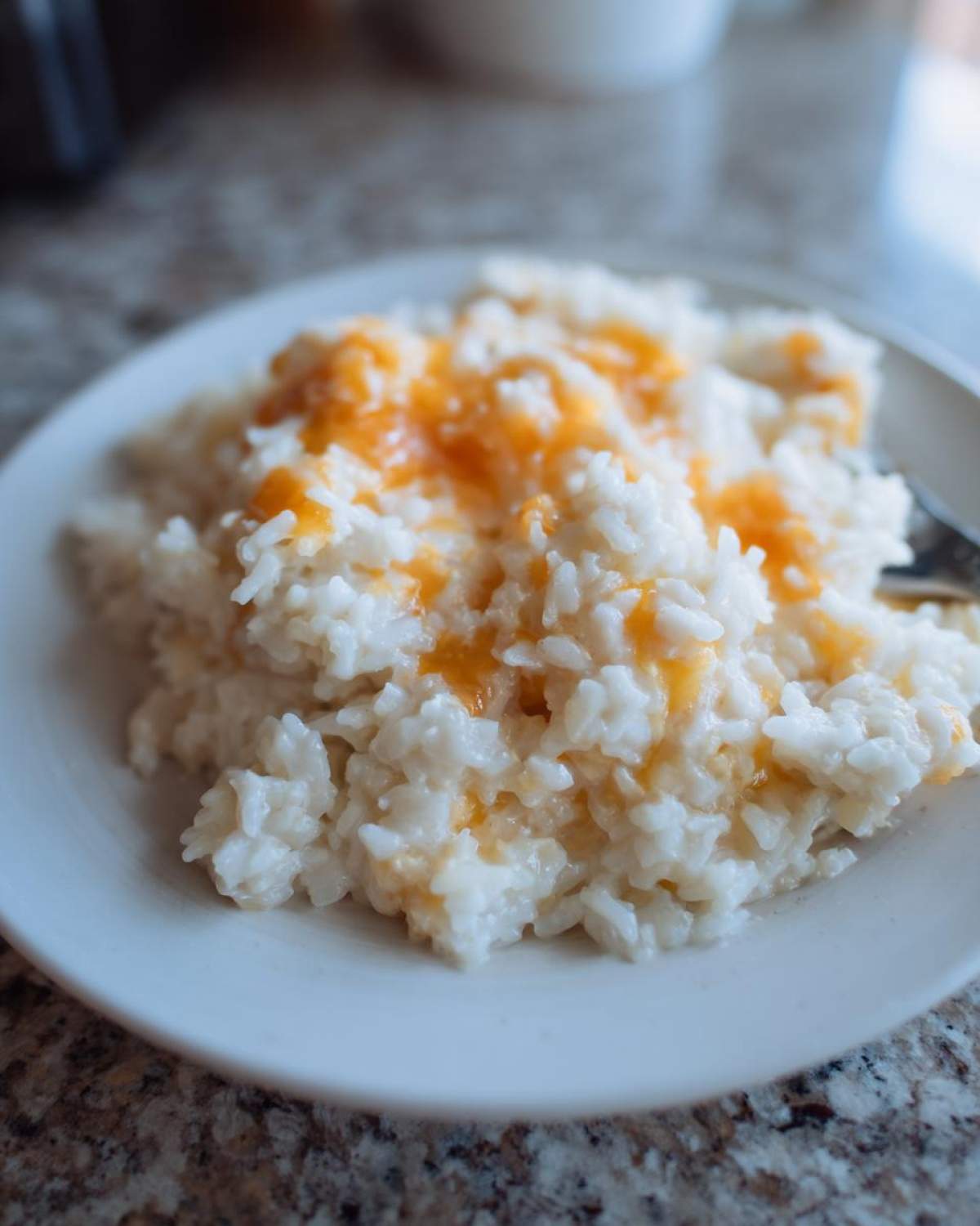 Close-up of a white plate holding a serving of creamy, white cheesy rice topped with melted orange cheddar cheese.
