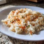 A close-up of a white bowl filled with amazing cheesy rice, featuring melted orange cheese and green parsley flecks.