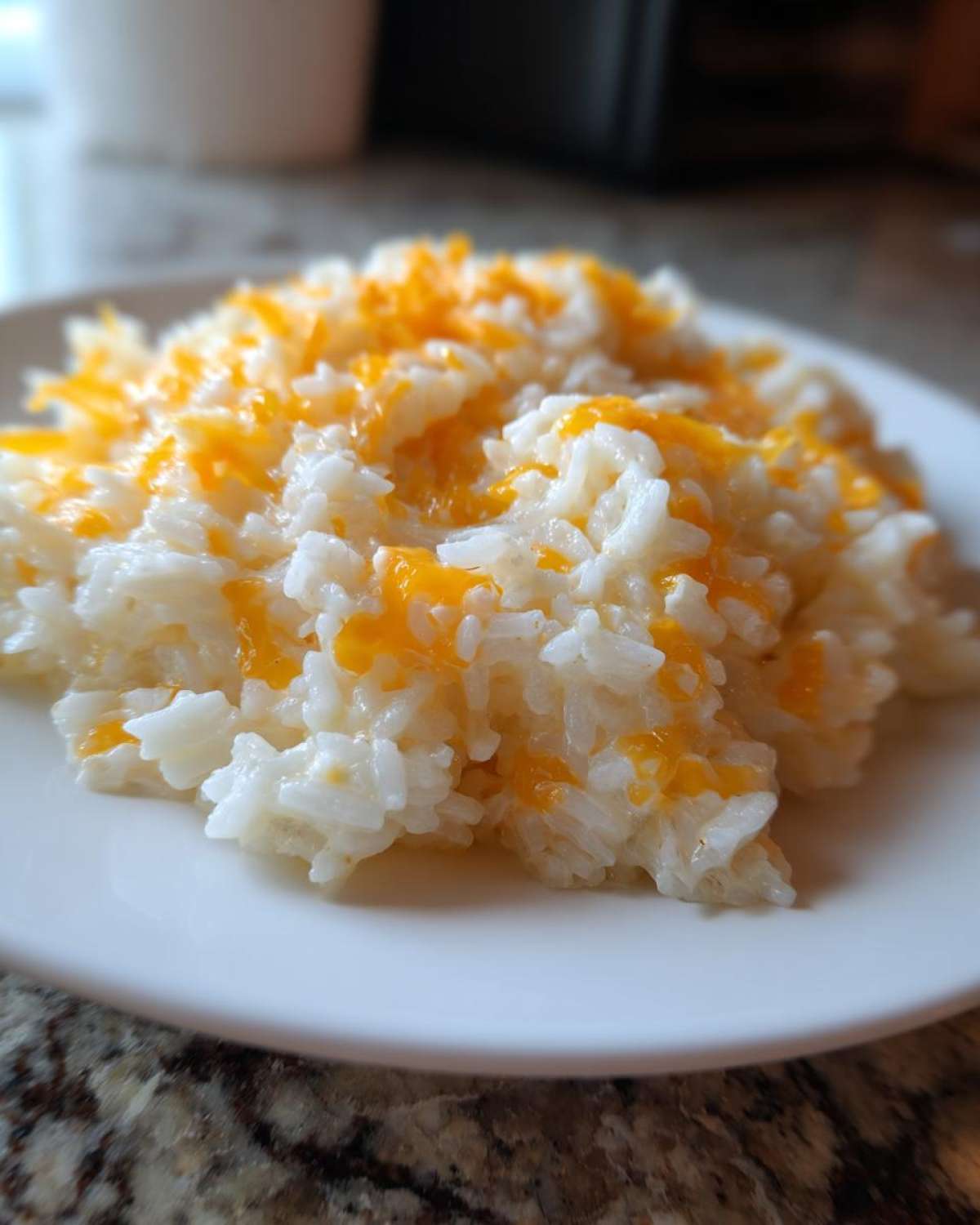 A close-up of a serving of amazing cheesy rice topped with melted orange cheddar cheese on a white plate.