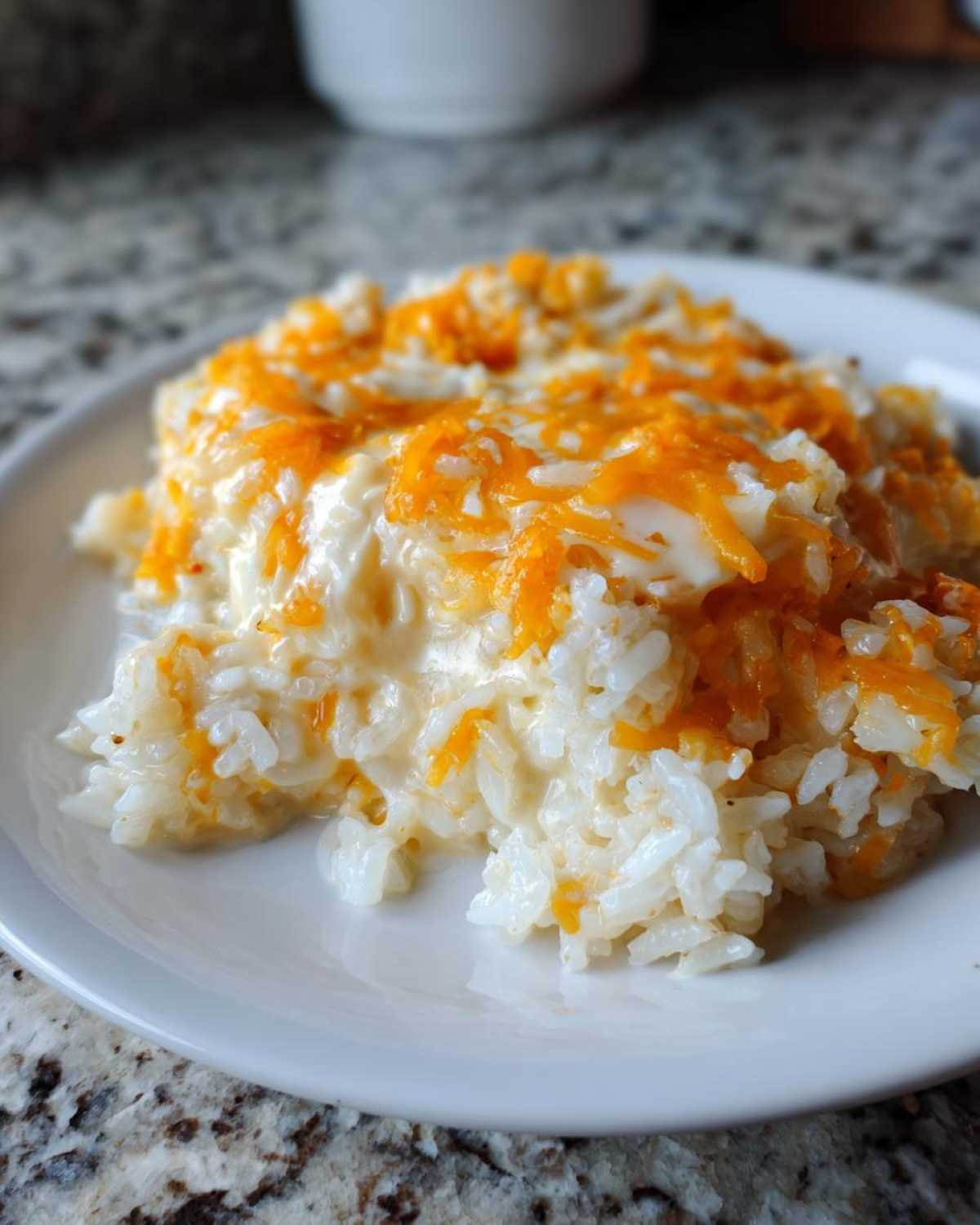 A close-up serving of amazing cheesy rice mixed with a creamy sauce and topped with melted shredded cheddar cheese.