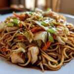A close-up of a plate piled high with glossy noodles, chicken pieces, cabbage, and carrots from the amazing chicken chow mein recipe.