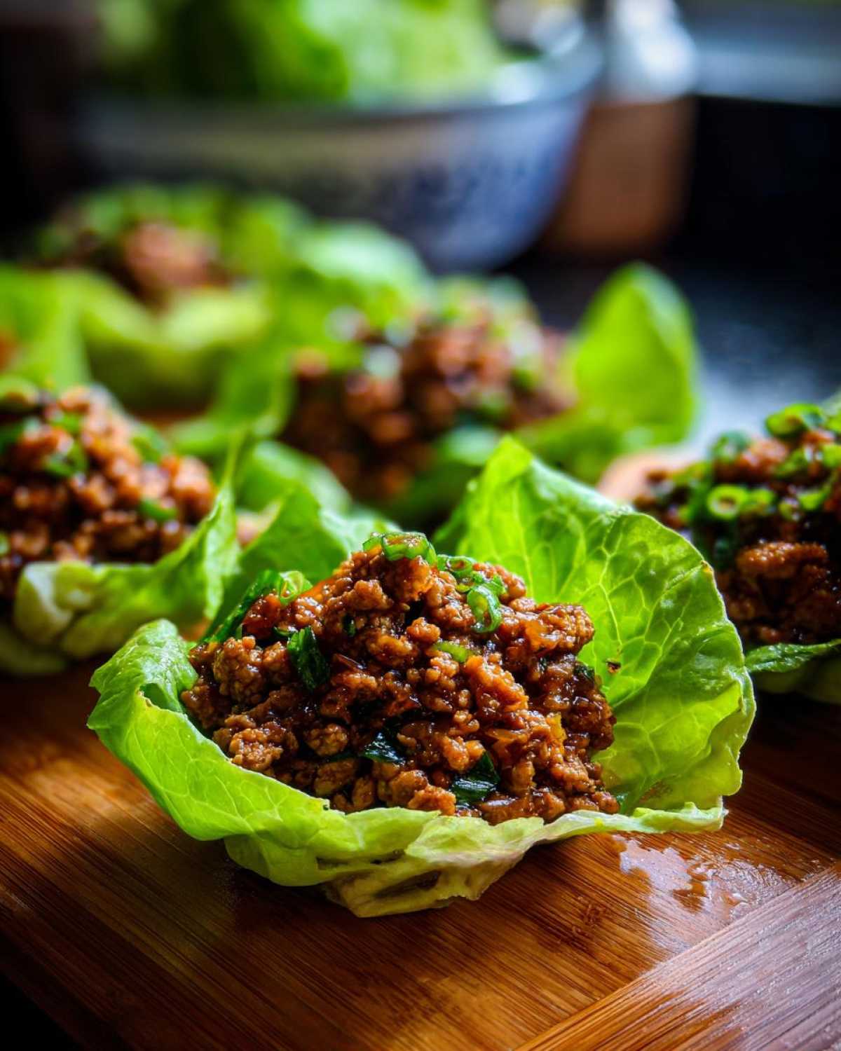 Close-up of savory filling served in crisp lettuce cups for chicken lettuce wraps, garnished with green onions.