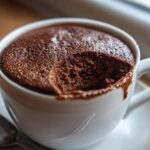 Close-up of rich, dark chocolate mousse with a spoonful taken out, served in a white mug.