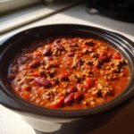 Close-up of rich, red crockpot chili featuring ground beef and kidney beans, simmering in a dark slow cooker insert.