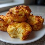 A stack of fluffy, golden brown baked egg bites on a white plate, one bite has a piece taken out.