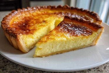 A slice of golden brown egg custard tart resting next to the main tart on a white plate.