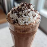A tall glass of amazing frozen hot chocolate topped with whipped cream and chocolate shavings.