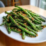 A mound of bright green beans tossed with crispy, golden brown breadcrumbs served on a white plate.
