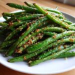 A close-up of bright green beans seasoned and topped with crispy brown breadcrumbs.