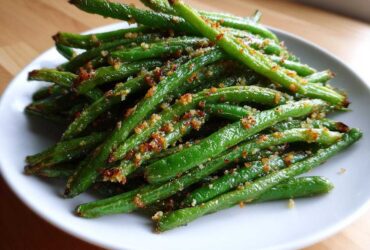 A close-up of bright green beans seasoned and topped with crispy brown breadcrumbs.