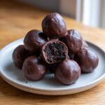 A stack of rich, chocolate-dipped Oreo balls, with one cut open to show the dark, crumbly interior.