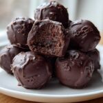 A stack of homemade chocolate coated Oreo balls, with one cut open showing the dark, dense center.