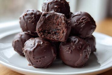 A stack of homemade chocolate coated Oreo balls, with one cut open showing the dark, dense center.