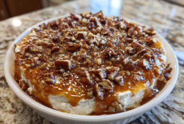 A close-up of the amazing pecan pie dip, featuring a creamy base topped with gooey caramel sauce and chopped pecans.