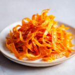 Close-up of a vibrant raw carrot salad made with shaved carrot ribbons, topped with sesame seeds.