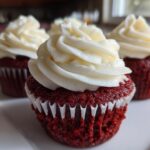 Close-up of three moist red velvet cupcakes topped with thick swirls of cream cheese frosting.