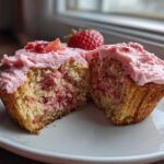 A strawberry cupcake cut in half showing the moist interior with strawberry pieces and pink frosting.