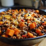 Close-up of a savory sweet potato skillet featuring ground meat, black beans, and melted cheese in a cast iron pan.