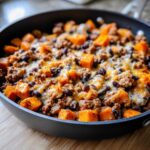 Close-up of a savory sweet potato skillet featuring diced sweet potatoes, ground meat, black beans, and melted cheese.