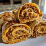 Close-up of several baked taco pinwheels showing the swirl of seasoned ground beef and melted cheese filling.
